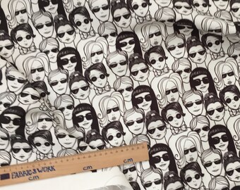 May include: Black and white fabric with a repeating pattern of stylized faces wearing sunglasses. The fabric is on a white surface with a wooden ruler.