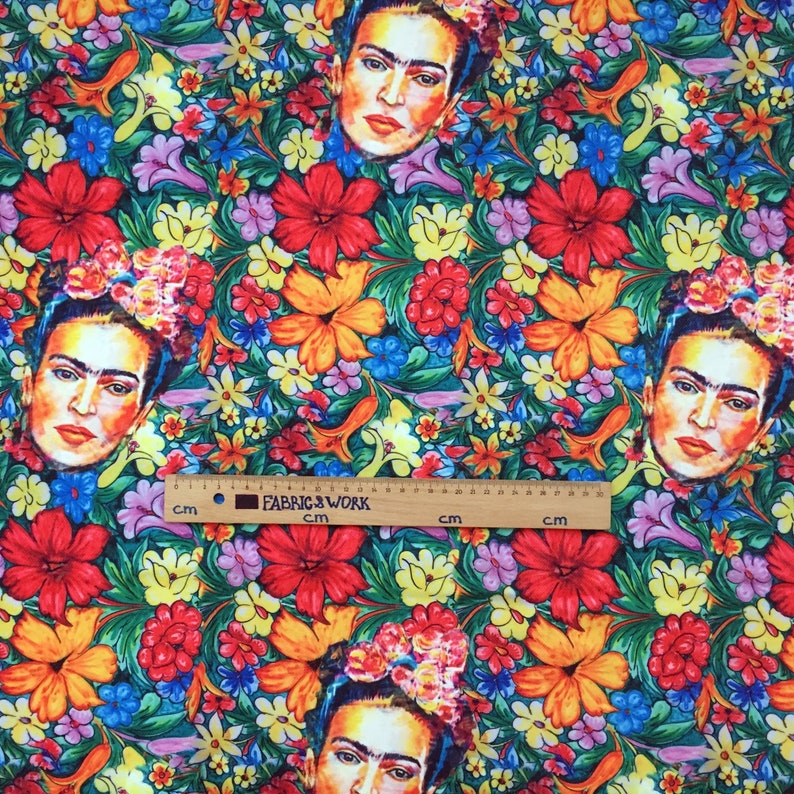 Op de afbeelding: Een kleurrijke stof met een herhalend patroon van Frida Kahlo's gezicht en felle bloemen. De stof is groen, rood, geel, oranje, blauw en roze.