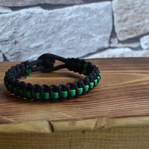 May include: A black and green paracord bracelet with a knot closure.