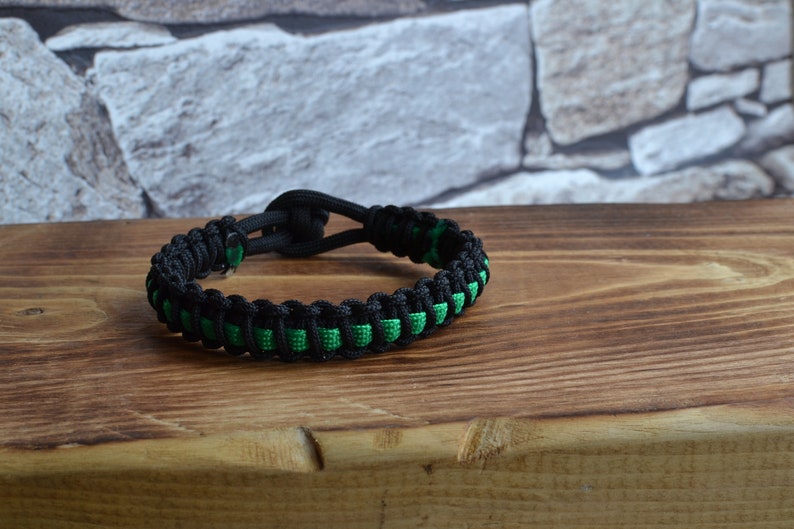 May include: A black and green paracord bracelet with a knot closure.
