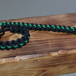 May include: Two black and green paracord bracelets. One bracelet is tied in a circle, the other is laid out straight.