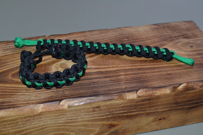 May include: Two black and green paracord bracelets. One bracelet is tied in a circle, the other is laid out straight.