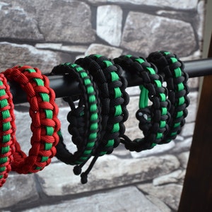 May include: Five paracord bracelets in black, green, and red. The bracelets are displayed on a black metal rod.