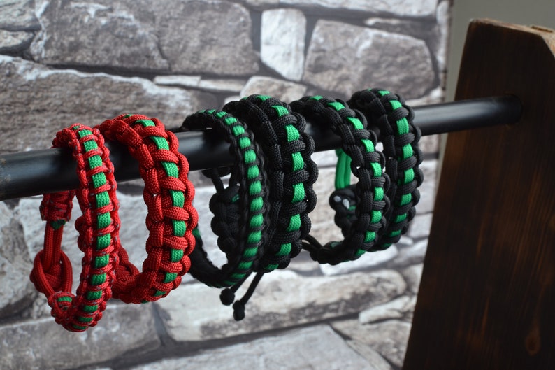 May include: Five paracord bracelets in black, green, and red. The bracelets are displayed on a black metal rod.