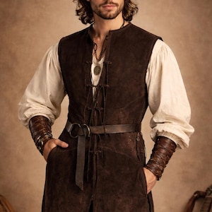 May include: A brown suede vest with a matching belt and leather wrist cuffs. The vest is layered over a white long-sleeve shirt. The outfit has a medieval or renaissance theme.