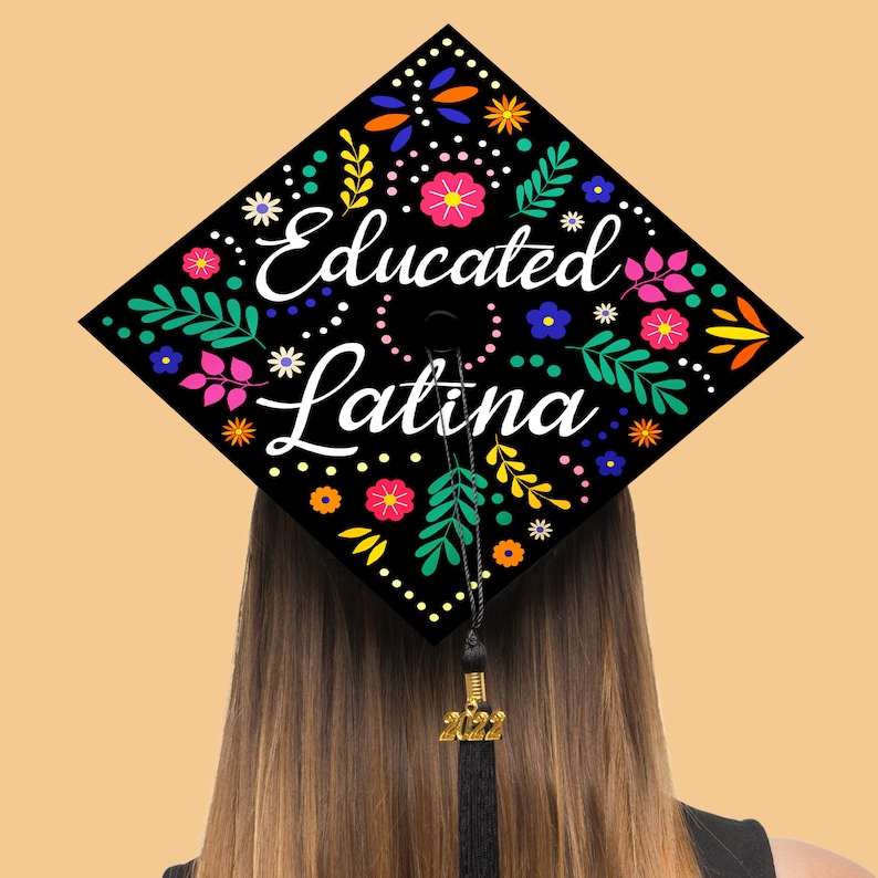 May include: Black graduation cap with a floral design and the text "Educated Latina" in white. The cap has a gold tassel with the year 2022.