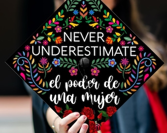 May include: Black graduation cap with colorful floral embroidery and the text "Never underestimate el poder de una mujer" in white.