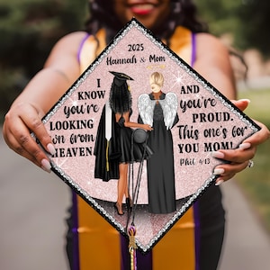 May include: A pink and black graduation cap with rhinestones. The cap features an illustration of two women, one in a graduation gown and the other with angel wings. The text on the cap reads "I know you're looking down from heaven 2025 Hannah & Mom AND you're PROUD. This one's for YOU MOM! Phil 4:13"