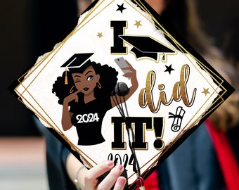 May include: A white graduation cap with a gold border and black and gold stars. The cap features a black and white illustration of a woman taking a selfie with the text "I did it!" in gold lettering. The year 2024 is printed on the cap.