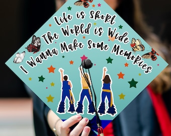 May include: A graduation cap with a light blue background featuring the text "Life is Short, The World is Wide, I Wanna Make Some Memories." The cap has illustrations of butterflies and figures, with colorful stars. A black tassel hangs from the cap.