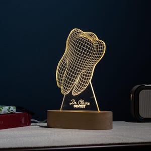 May include: A wooden base with a 3D printed tooth design lamp with the text "Dr. Claire DENTIST" on the front.