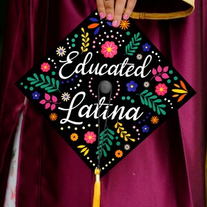 May include: A black graduation cap with a colorful floral design and the text "Educated Latina" in white.
