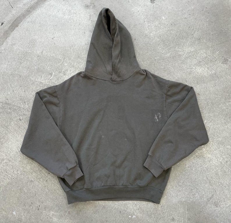 May include: A dark gray hoodie with a hood and long sleeves. The sweatshirt has a small, faded design on the chest. The garment is made of a soft material and is suitable for casual wear.
