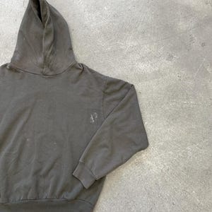 May include: A dark gray hoodie with a drawstring hood and long sleeves. The sweatshirt has a small, faded design on the left chest area. The fabric appears to be a soft, worn material, suggesting comfort and casual wear.