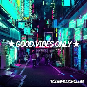 May include: A neon-lit city street at night with the text "GOOD VIBES ONLY" in white letters with a star on each side. The text is in front of a blurred background of people walking in the street. The text "TOUGHLUCKCLUB" is at the bottom of the image.