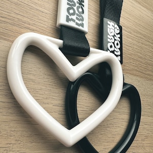 May include: White and black heart-shaped keychains with the text "TOUGH" and "HERO" printed on them.