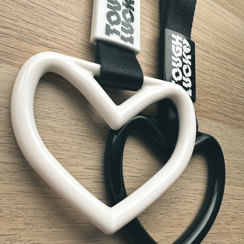 May include: White and black heart-shaped keychains with the text "TOUGH" and "HERO" printed on them.