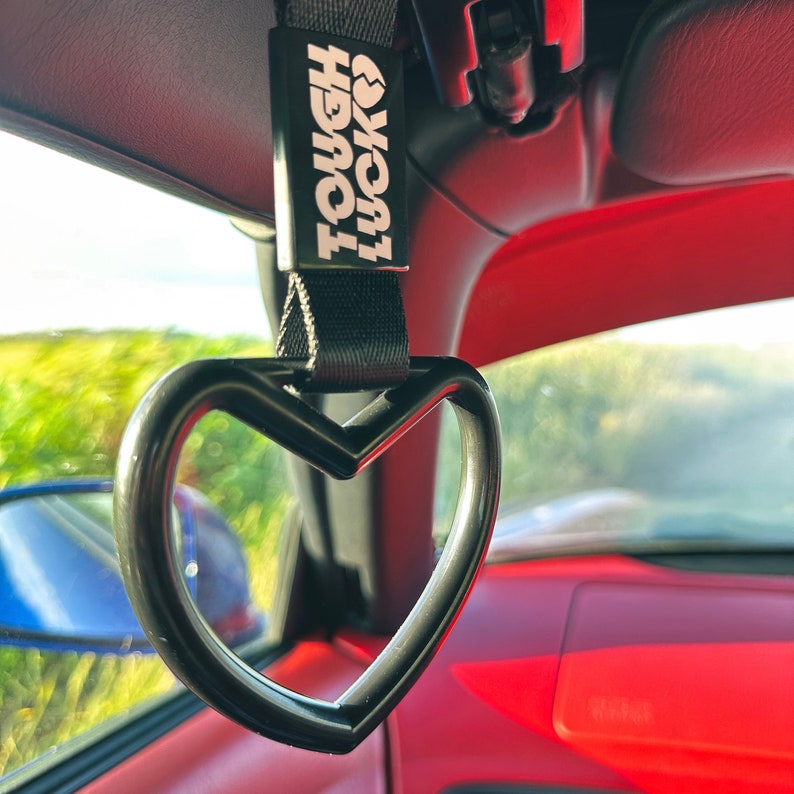 May include: A black heart-shaped car handle with a black strap and a white tag that reads "Tough Luck".