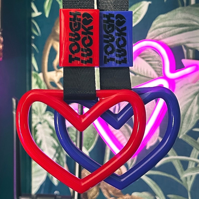 May include: Two red and blue heart-shaped keychains with black straps. The keychains have the text "Tough Luck" printed on them.