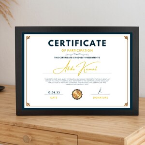 Peut inclure: Un certificat encadré noir avec un sceau doré et des accents bleus. Le certificat est pour la participation à une formation en design graphique et est remis à "Abde Kamal". La date sur le certificat est le 12.08.22.