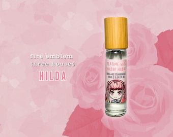 May include: A clear glass roll-on fragrance bottle with a wooden cap. The label features a cartoon illustration of a character with pink hair and the text "Teatime with Hilda! Hilda!" on a pink floral background. The background is a pink gradient with rose illustrations.