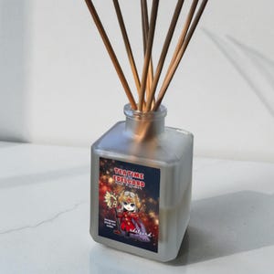 May include: A frosted glass diffuser bottle with wooden reeds. The label reads "TEATIME EDELGARD" and features a cartoon character in red and gold. The diffuser is likely scented with bergamot, black tea, and cedar.