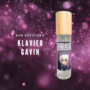 May include: A clear roll-on fragrance bottle with a wooden cap. The label features a cartoon character and the text "TOKEN OF MY PERFORMANCE". The background is a purple and pink galaxy design with the text "ace attorney KLAVIER GAVIN".