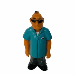 May include: A blue plastic figurine of a person wearing sunglasses and a blue shirt. The figurine has a mohawk hairstyle and is standing with its arms at its sides.