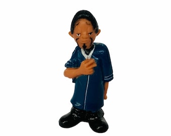 May include: A blue and white figurine of a man with a goatee and a serious expression. He is wearing a blue shirt with white trim and black trousers.