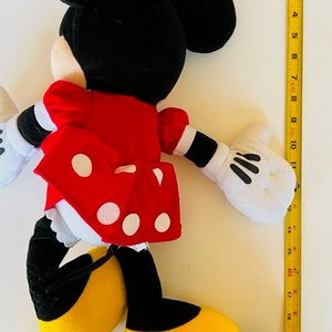May include: A plush toy of Minnie Mouse wearing a red dress with white polka dots and a black bow. She has black ears and yellow shoes.