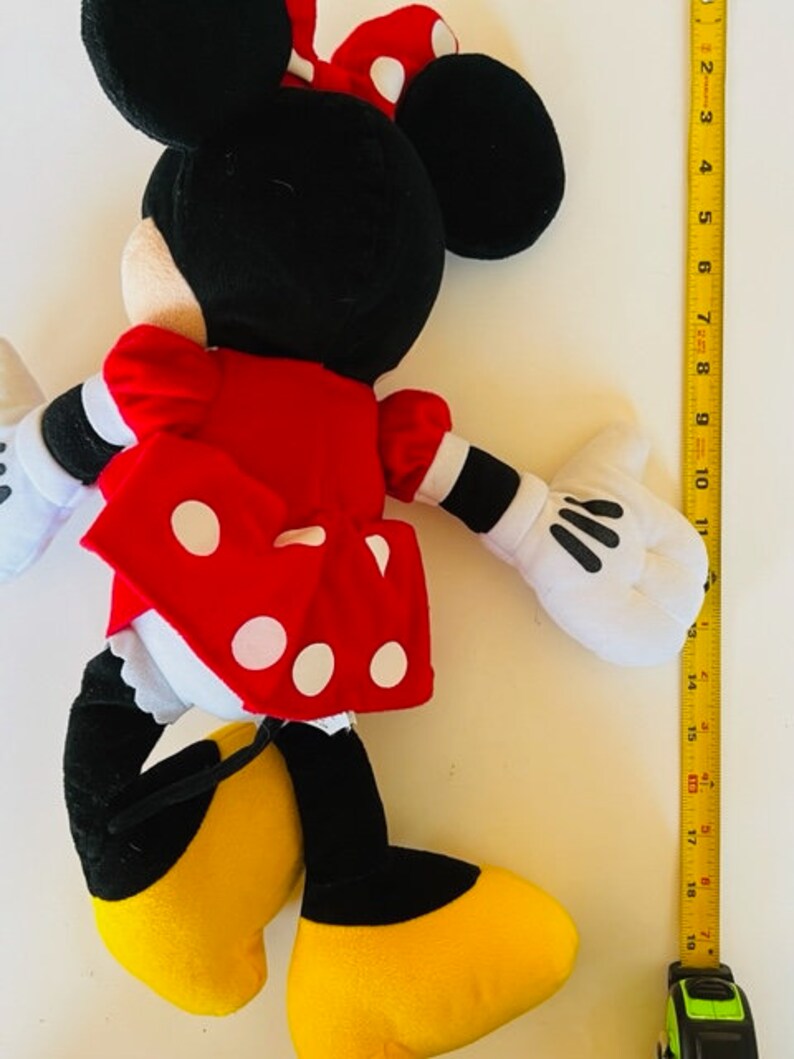 May include: A plush toy of Minnie Mouse wearing a red dress with white polka dots and a black bow. She has black ears and yellow shoes.