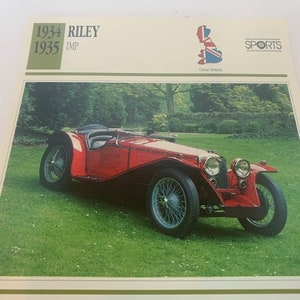May include: A red 1934-1935 Riley IMP sports car is parked on a grassy lawn. The car has a black leather interior and a chrome grille. The car is in excellent condition and is a classic example of a British sports car.