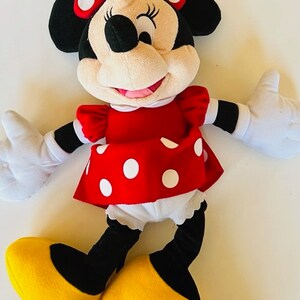 May include: A plush toy of Minnie Mouse wearing a red dress with white polka dots, a black bow with white polka dots, and yellow shoes.