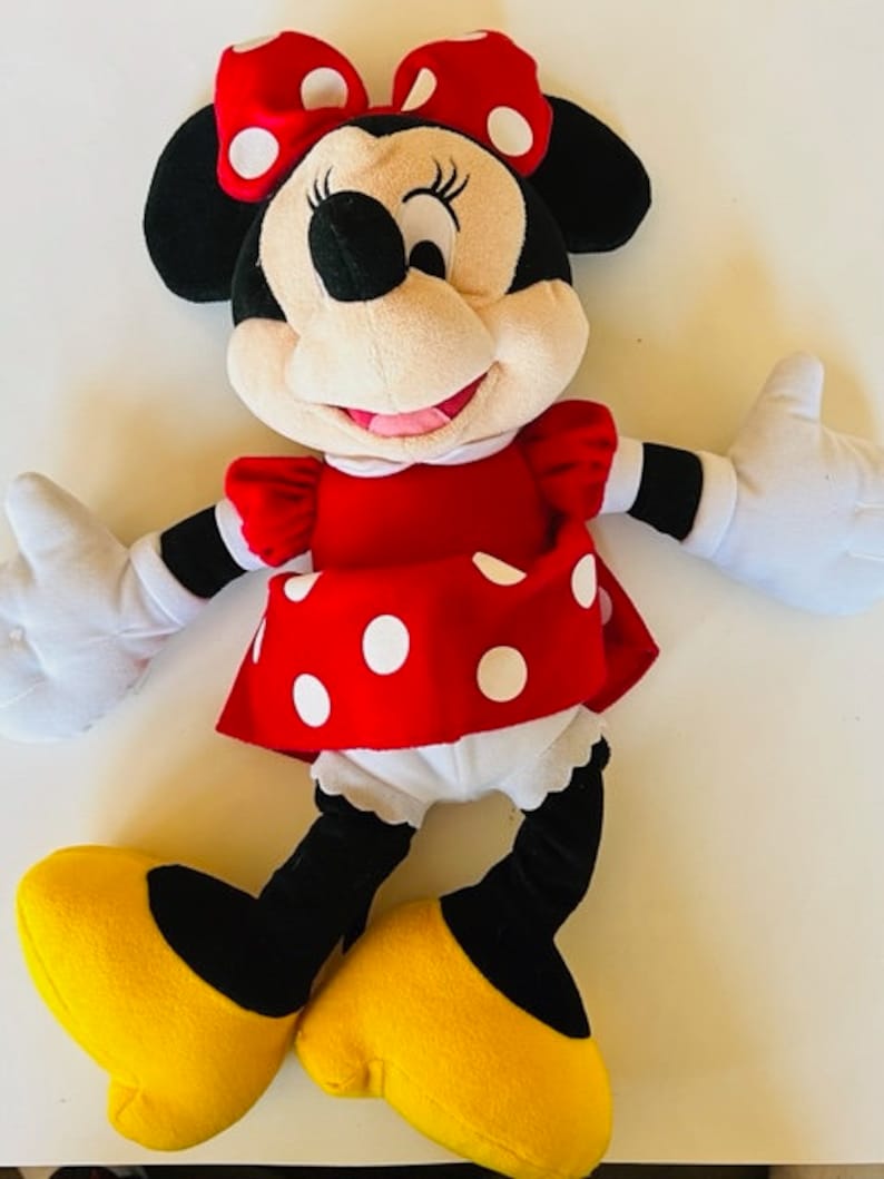 May include: A plush toy of Minnie Mouse wearing a red dress with white polka dots, a black bow with white polka dots, and yellow shoes.