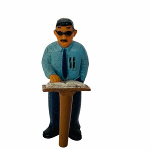 May include: A blue figurine of a person wearing sunglasses and a blue shirt with a tie, sitting at a wooden podium with a book on it.