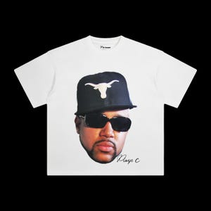 May include: White t-shirt with a black and white image of a man wearing a black hat with a white longhorn logo and sunglasses. The text "Pimp C" is printed in black below the image.