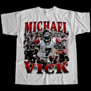 May include: White t-shirt featuring a graphic of a football player in a jersey with the number 7. The name "MICHAEL VICK" is printed in red, stylized text above and below the image of the player. Other players are also visible.