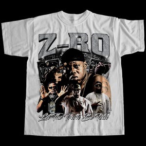 May include: White t-shirt with a graphic design. The design features the text "Z-RO" in a silver, textured font, and multiple images of a person. The phrase "Let The Truth Be Told" is in a script font.
