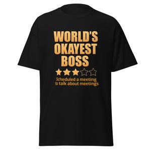 May include: Black t-shirt with the text "WORLD'S OKAYEST BOSS" in orange. Below the text are four gold stars and a half-star. The shirt also includes the text "Scheduled a meeting to talk about meetings."