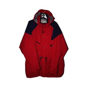 May include: A red and navy blue hooded jacket with a zip and button fastening. The jacket has a drawstring at the waist and a logo on the left chest.