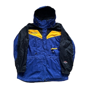 May include: Blue, black, and yellow Columbia hooded jacket. The jacket has a blue body with black sleeves and a black hood. Yellow accents are on the chest and shoulders. The Columbia logo is visible on the chest.