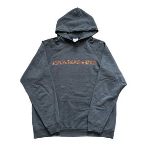 Puede incluir: Una sudadera con capucha gris oscuro con la palabra "RAMMSTEIN" impresa en el pecho en un dise&ntilde;o texturizado y multicolor. La sudadera tiene un bolsillo delantero y una capucha con cord&oacute;n. La prenda est&aacute; hecha de un material suave.