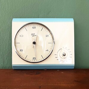 May include: A light blue vintage clock with a white face and silver hands. The clock has a timer dial on the right side. The clock face reads "Liberty Electric".