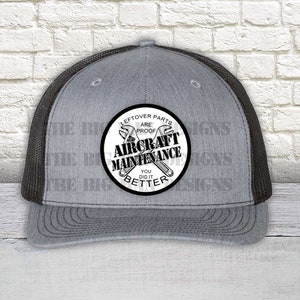 May include: A gray and black trucker hat with a white circle patch that says "Leftover parts are proof you did it better" with a wrench and a screwdriver crossed inside the circle. The text "Aircraft Maintenance" is written in a large font inside the circle.