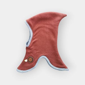 Puede incluir: Una capucha roja con capucha, ribete azul y una pequeña etiqueta marrón con la palabra "Lobo" en ella.