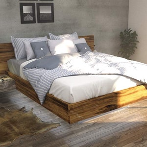 May include: A wooden bed frame with a white and gray striped comforter and pillows. The bed is in a bedroom with a concrete wall and a window with a view of trees.