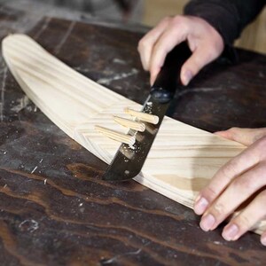 Puede incluir: Una persona utiliza una sierra de mano para cortar una pieza de madera. La madera se mantiene en su lugar mediante varias clavijas de madera.