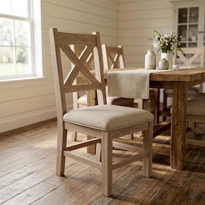 Może przedstawiać: Jasny drewniany krzesło do jadalni z oparciem w kształcie litery X i tapicerowanym siedziskiem. Krzesło jest częścią zestawu do jadalni, z drewnianym stołem i innymi krzesłami widocznymi w tle. Pokój ma neutralną paletę kolorów.