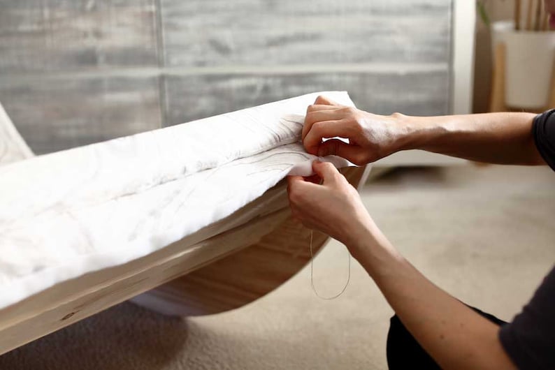 Puede incluir: Una persona cosiendo tela blanca a un marco de madera. La tela se est&aacute; tensando y la persona est&aacute; usando una aguja e hilo para sujetarla en su lugar.
