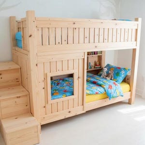 May include: A light-colored wooden bunk bed with a built-in staircase. The bed has a window and a small bookshelf. The bedding includes a yellow sheet, a blue comforter, and a blue pillow with a cartoon design.